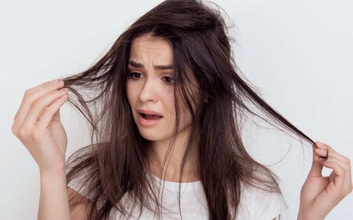 Mulher observando a queda de fios ao passar a mão pelo cabelo.